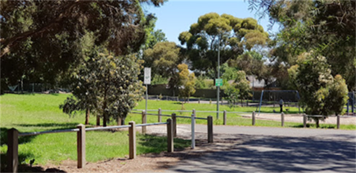 Green open space next to a small local playground. Surrounded by large green trees